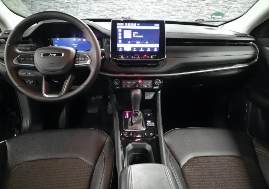 Intérieur noir du Jeep Compass 2024 vu de face, avec tableau de bord numérique et écran tactile central lumineux.