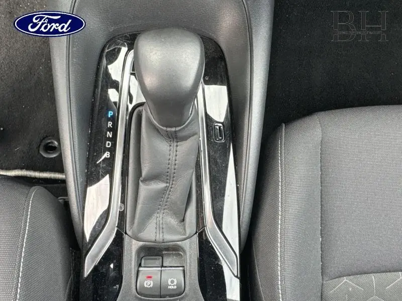 Gros plan sur le levier de vitesses automatique noir et la console centrale avec sièges en tissu gris à droite.