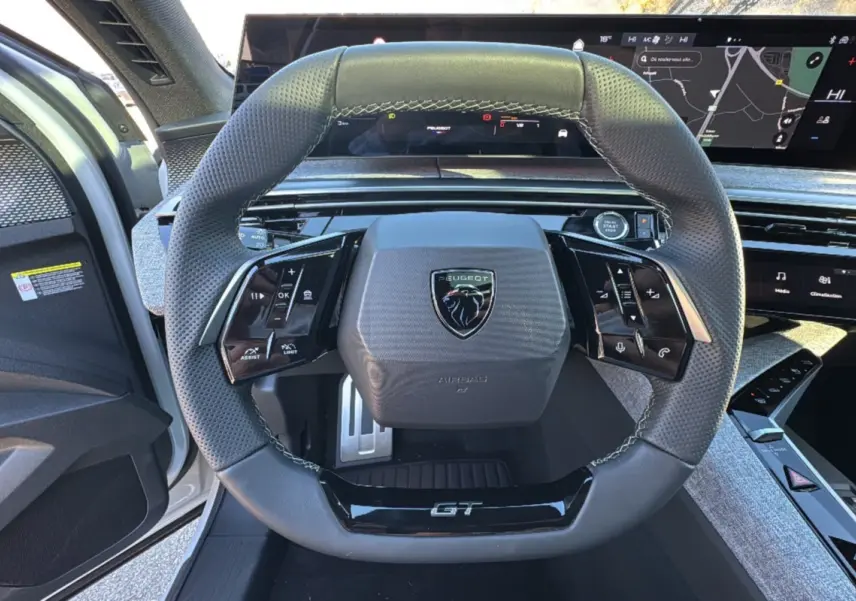 Vue rapprochée du volant cuir perforé GT avec commandes intégrées et tableau de bord numérique du Peugeot 3008 hybride 2025.