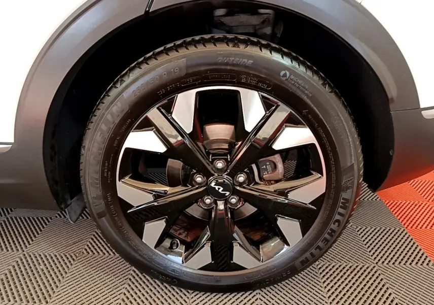 Gros plan sur la roue avant droite du KIA SPORTAGE blanc, avec jante noire et argentée au design moderne.