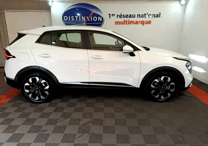 Vue de profil côté gauche d’un KIA SPORTAGE blanc 2022 hybride rechargeable avec jantes noires et rails de toit noirs.