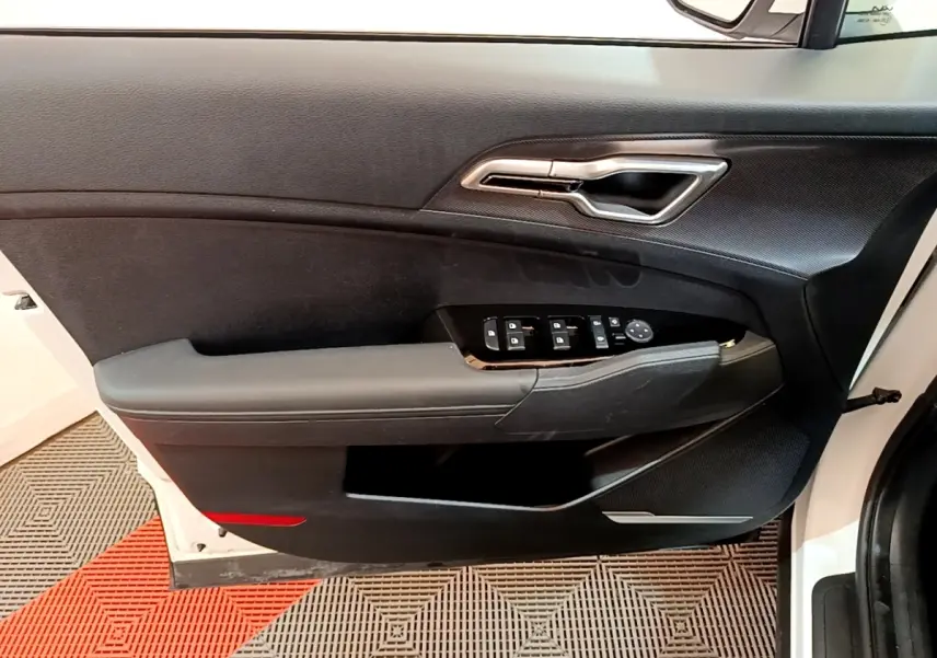 Vue intérieure de la porte avant gauche blanche du KIA SPORTAGE 2022 avec commandes électriques et poignée chromée.