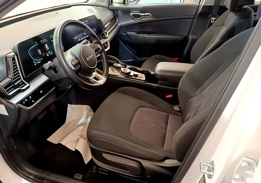 Intérieur côté conducteur du Kia Sportage blanc 2022, avec tableau de bord digital et sièges noirs en tissu.