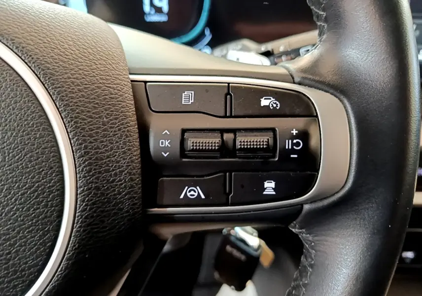 Gros plan sur les commandes multifonctions noires du volant en cuir noir du Kia Sportage blanc, version hybride rechargeable.