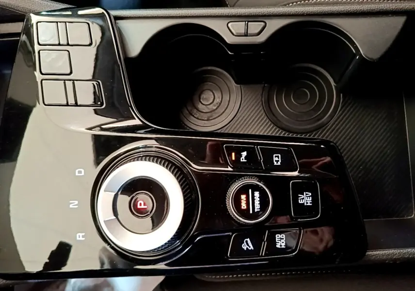 Gros plan sur la console centrale noire du Kia Sportage hybride rechargeable, avec sélecteur rotatif de boîte auto et boutons de contrôle.