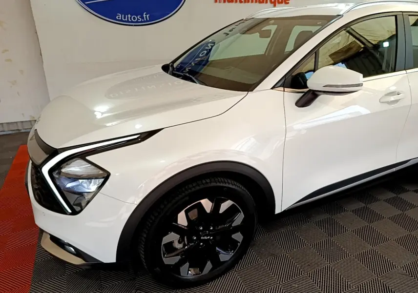 Vue 3/4 avant droit du KIA SPORTAGE blanc avec phares LED en forme de boomerang et jantes noires distinctives.