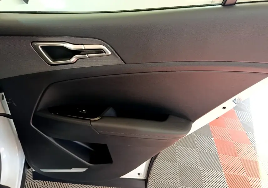Vue intérieure côté gauche de la porte avant d’un KIA SPORTAGE blanc avec poignée argentée et accoudoir noir.