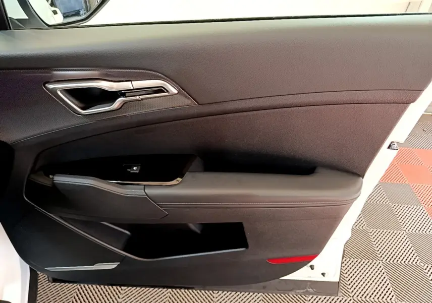 Vue intérieure côté gauche de la porte avant noire d’un Kia Sportage blanc avec poignée argentée et commande de fenêtre.
