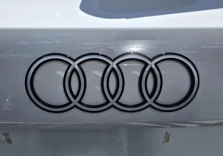 Gros plan sur le logo Audi noir brillant sur la carrosserie blanche Arkona d'une Audi A3 Sportback 2024.