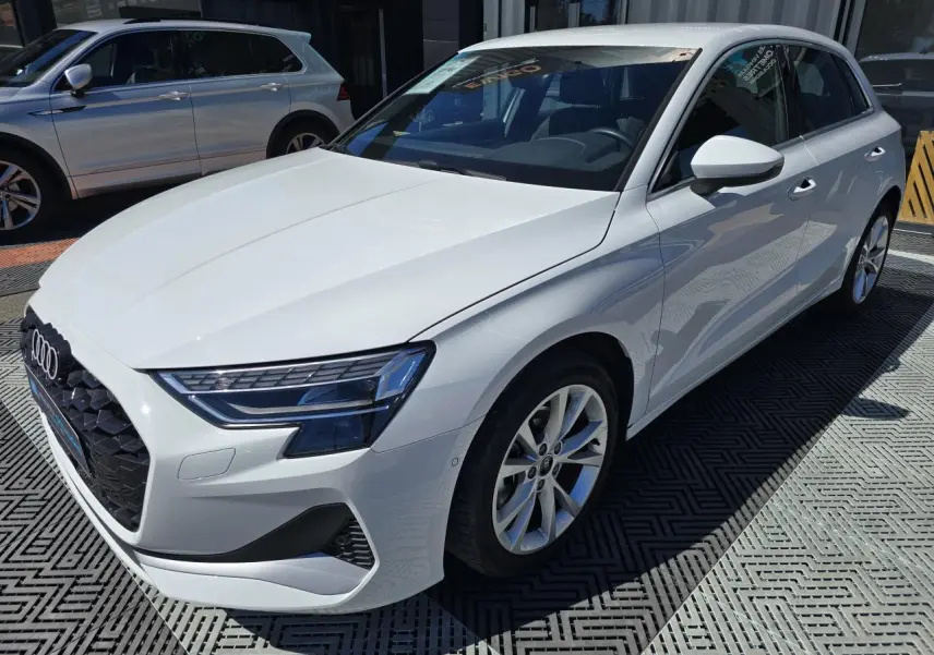Audi A3 Sportback blanc Arkona vue 3/4 avant droit, avec jantes alliage 5 branches et phares LED distinctifs.