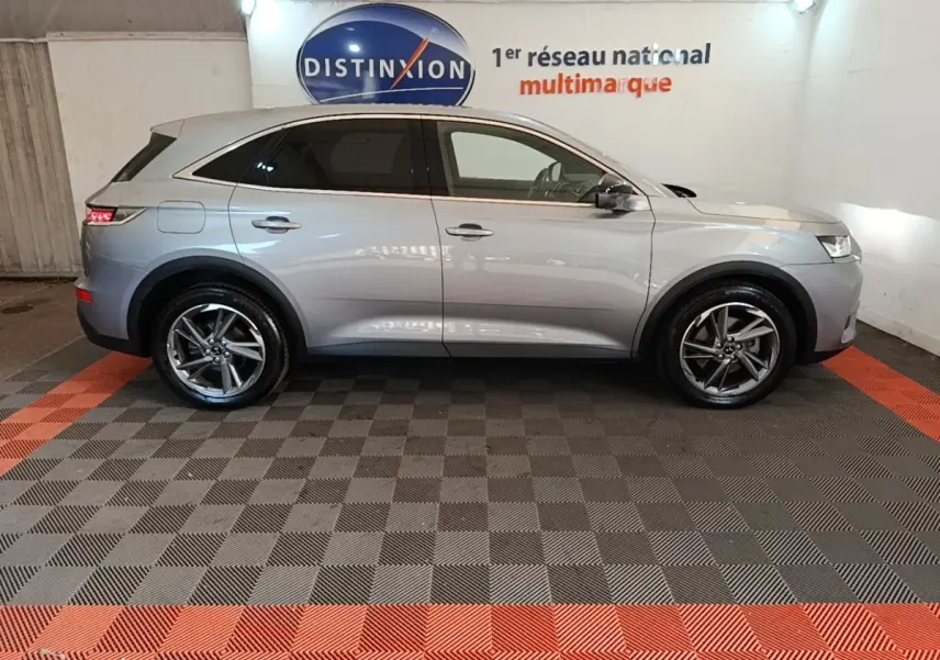 Vue de profil côté gauche d’un DS7 Crossback E-TENSE 225 Business gris foncé en intérieur sur sol damier noir et rouge.