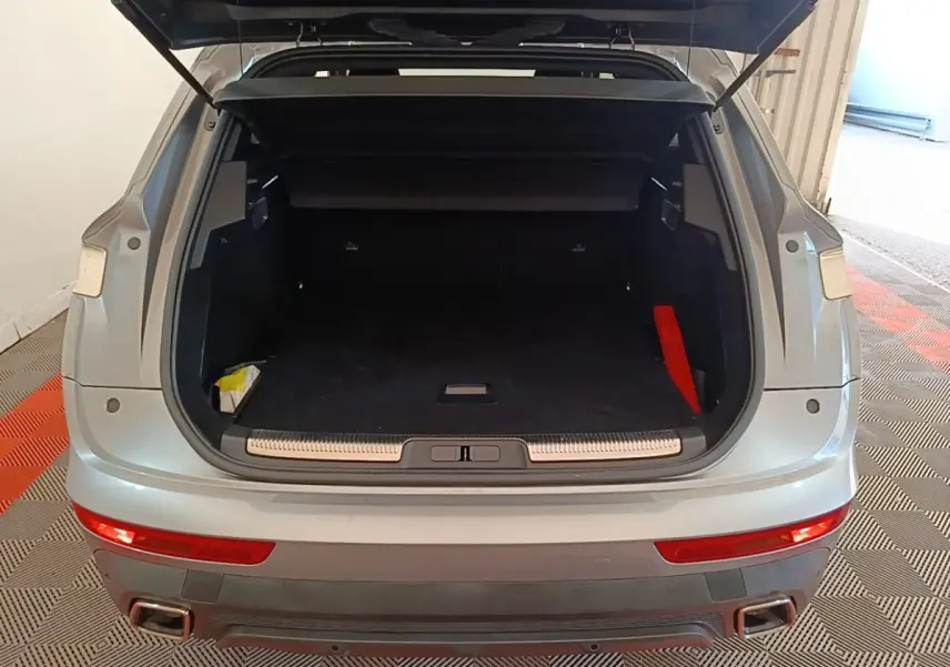 Vue arrière du coffre ouvert du DS7 Crossback gris foncé, montrant l'espace de chargement vide et les feux arrière allongés.