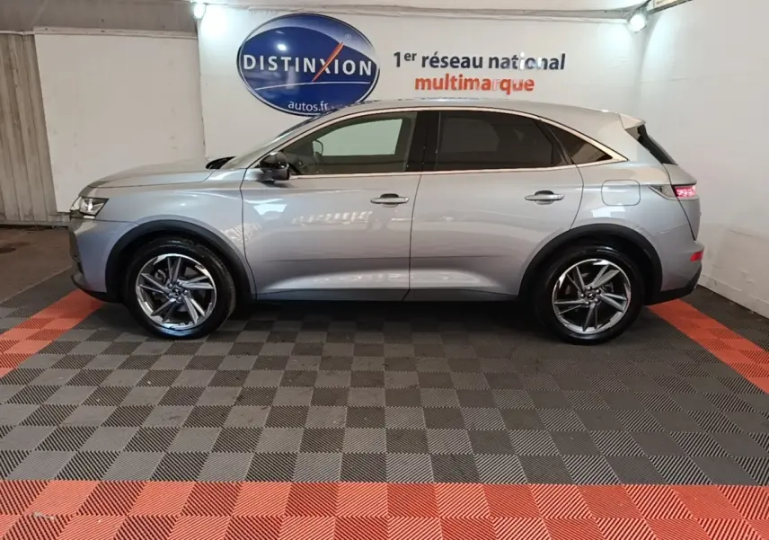 Vue latérale droite d’un DS7 Crossback gris foncé avec jantes alliage et feux arrière LED allumés en intérieur showroom.