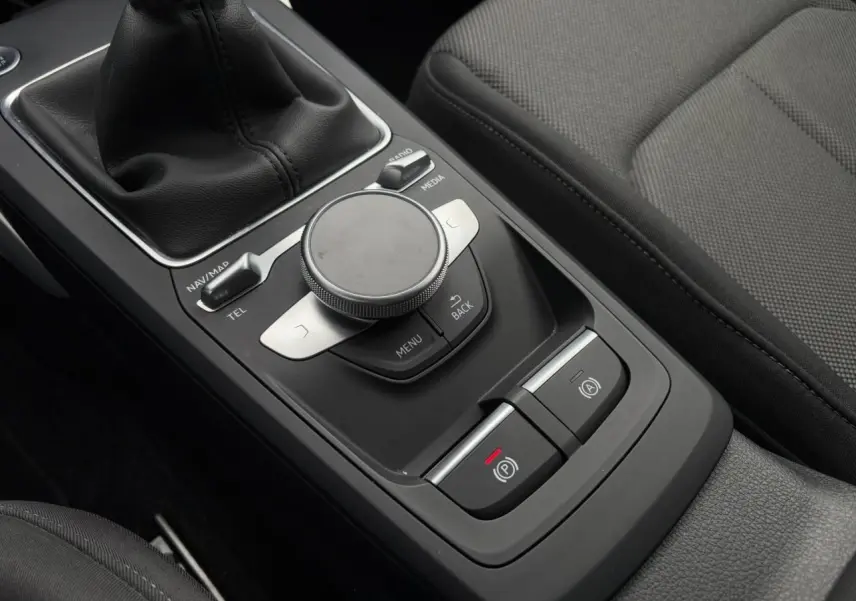 Gros plan sur la console centrale noire de l'Audi Q2 30 TFSI S-Line avec commande MMI et frein à main électronique.