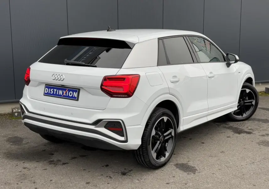 Audi Q2 30 TFSI S-Line blanc Glacier vue 3/4 arrière droit avec jantes noires et vitres surteintées.