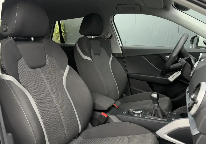 Vue intérieure de l’Audi Q2 30 TFSI S-Line 2024 montrant les sièges sport avant en tissu gris et la console centrale avec levier de vitesse manuel.