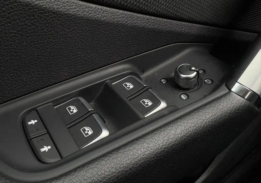 Gros plan sur les commandes de lève-vitres et réglage des rétroviseurs côté conducteur de l'Audi Q2 30 TFSI blanc Glacier.