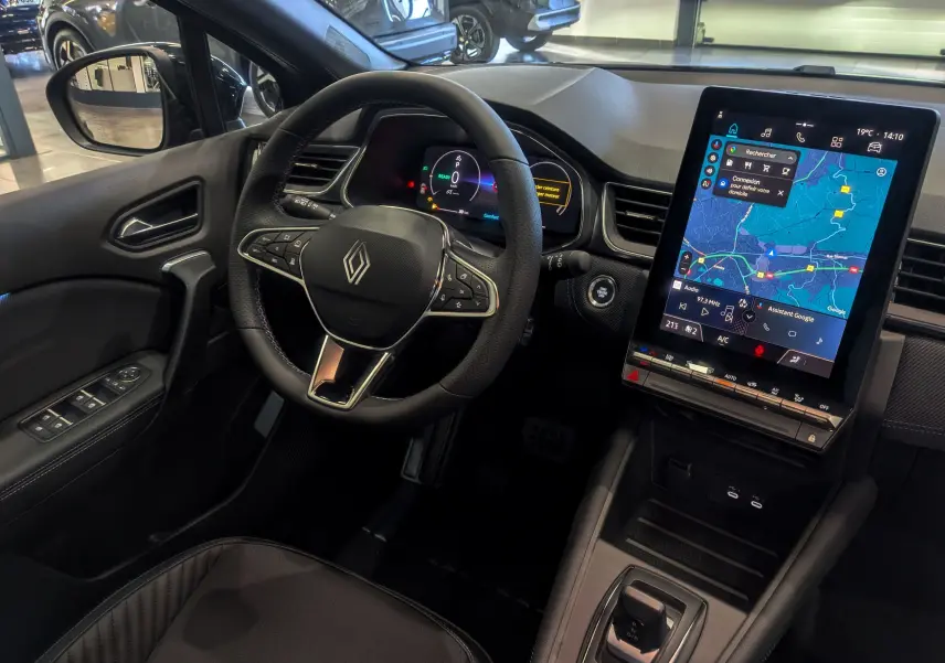 Intérieur avant du Renault Captur E-TECH 2025, volant multifonction et grand écran tactile avec navigation visible.