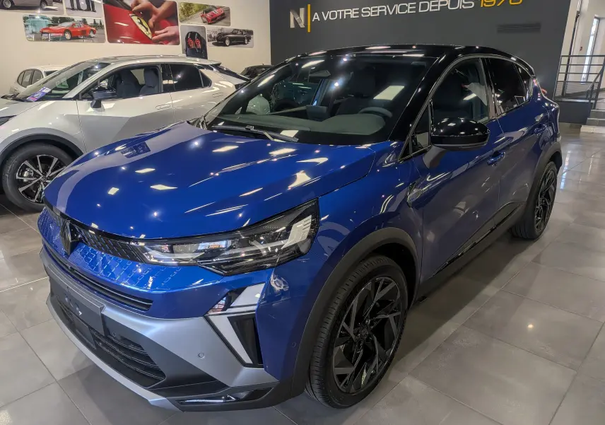 Renault Captur E-TECH hybride 2025 bleu Iron avec toit noir, vue 3/4 avant droit en showroom lumineux.