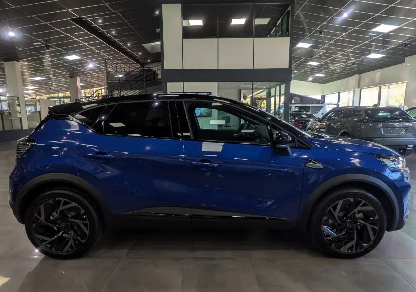 Profil côté gauche du Renault Captur E-TECH 160 esprit Alpine bleu Iron avec toit noir et jantes noires en showroom.