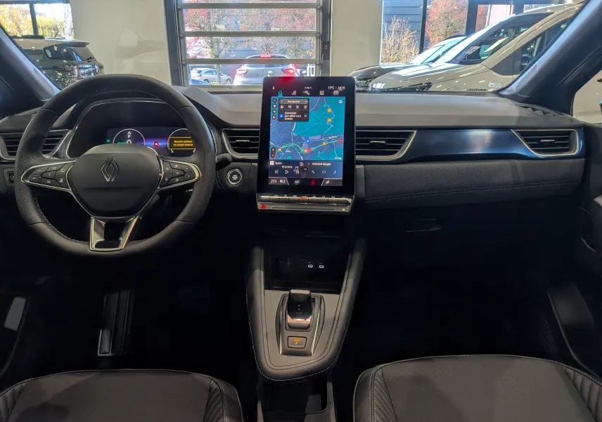 Vue intérieure frontale du tableau de bord du Renault Captur E-Tech 2025 avec écran tactile central et volant multifonction noir.