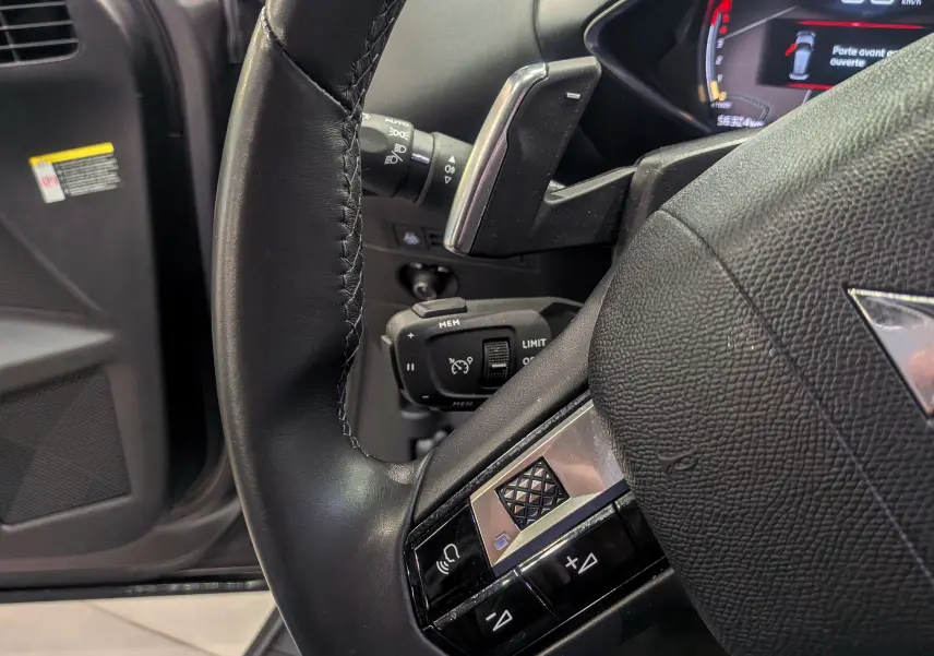 Gros plan sur le volant en cuir noir du DS3 Crossback 2022 avec commandes intégrées et tableau de bord partiellement visible.