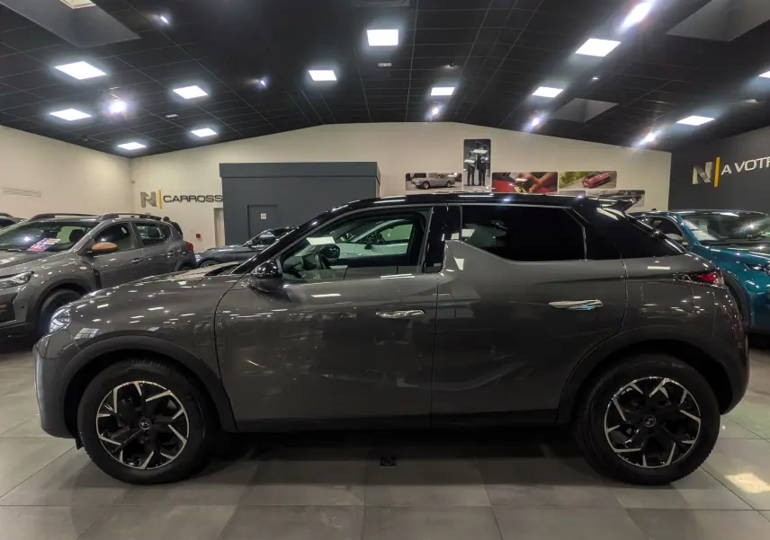 Vue de profil côté gauche du DS3 Crossback gris Platinium avec toit noir dans un showroom lumineux.