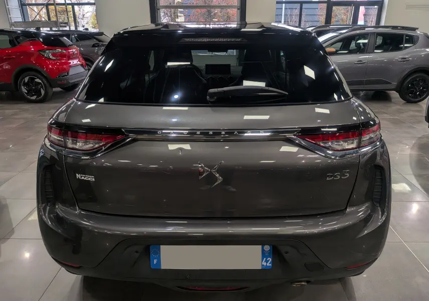 Vue arrière d'un DS3 Crossback gris Platinium avec toit noir, mettant en valeur son logo DS et ses feux LED fins.