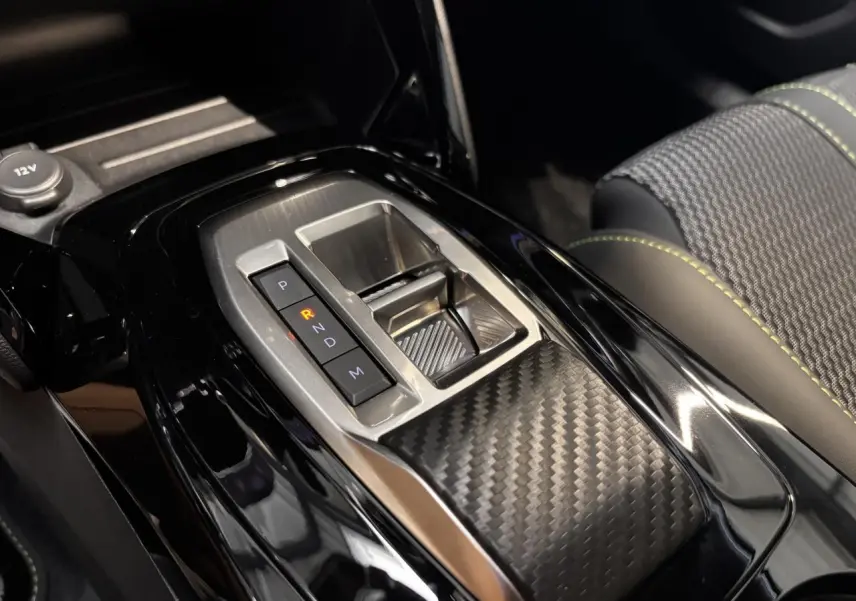 Gros plan sur la console centrale du Peugeot 2008 blanc 2025, mettant en valeur la boîte automatique et les surpiqûres vertes des sièges.