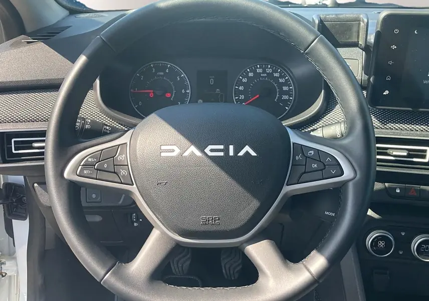 Vue rapprochée du volant noir de la Dacia Sandero 2025 avec commandes intégrées et tableau de bord visible.