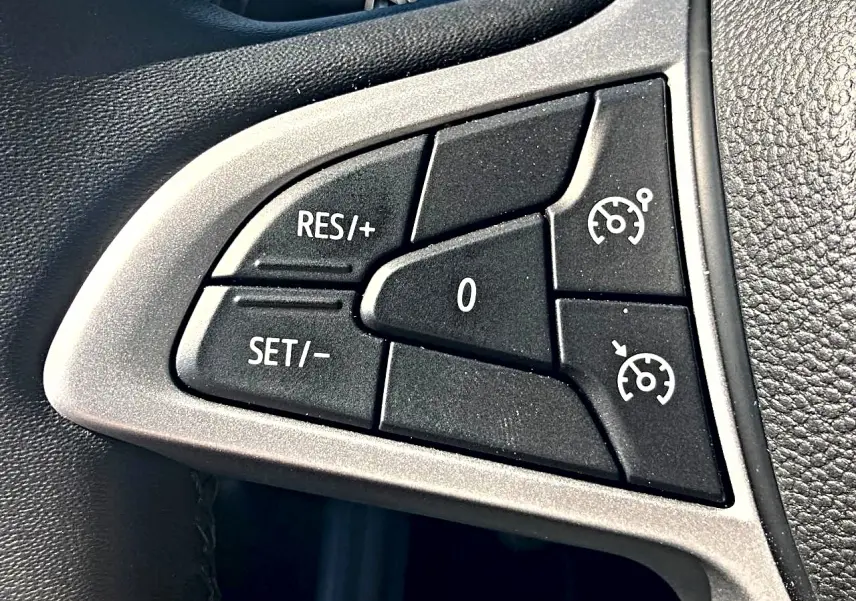 Gros plan sur les commandes noires du régulateur de vitesse sur le volant gris et noir d’une Dacia Sandero blanche.