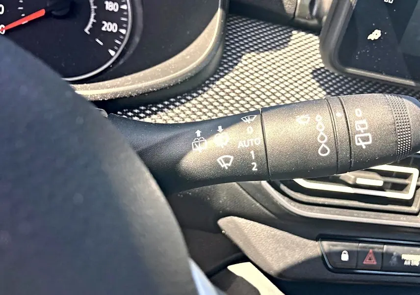 Gros plan sur la commande d’essuie-glace à gauche du volant dans l’habitacle noir d’une Dacia Sandero blanche 2025.