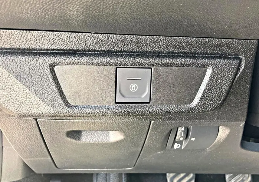 Gros plan sur le bouton de verrouillage centralisé noir sur le tableau de bord noir de la Dacia Sandero blanche.
