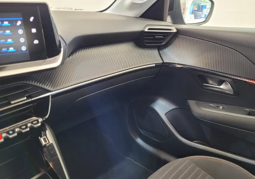 Vue intérieure côté passager du tableau de bord et porte avec finition noire et détails en fibre de carbone du Peugeot 208 2023.