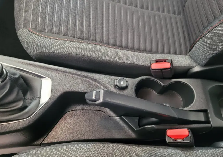 Vue rapprochée de la console centrale et frein à main d'une Peugeot 208 gris foncé avec sièges tissu gris et coutures rouges.