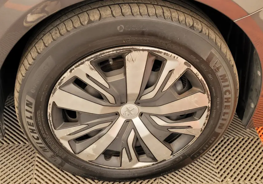 Gros plan sur la roue avant gauche d'une Peugeot 208 gris foncé avec jante en alliage au design moderne.