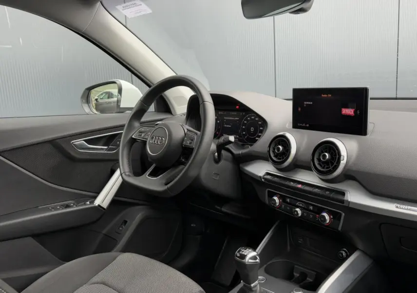 Vue intérieure côté conducteur de l'Audi Q2 30 TFSI S-Line 2024 avec tableau de bord noir et écran central.