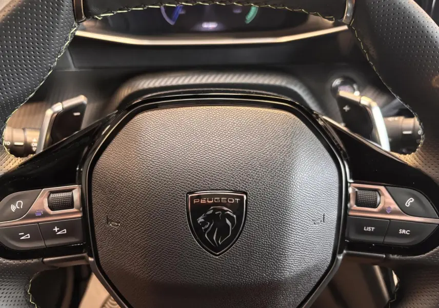 Gros plan sur le volant noir perforé du Peugeot 2008 gris, avec commandes intégrées et logo lion central.