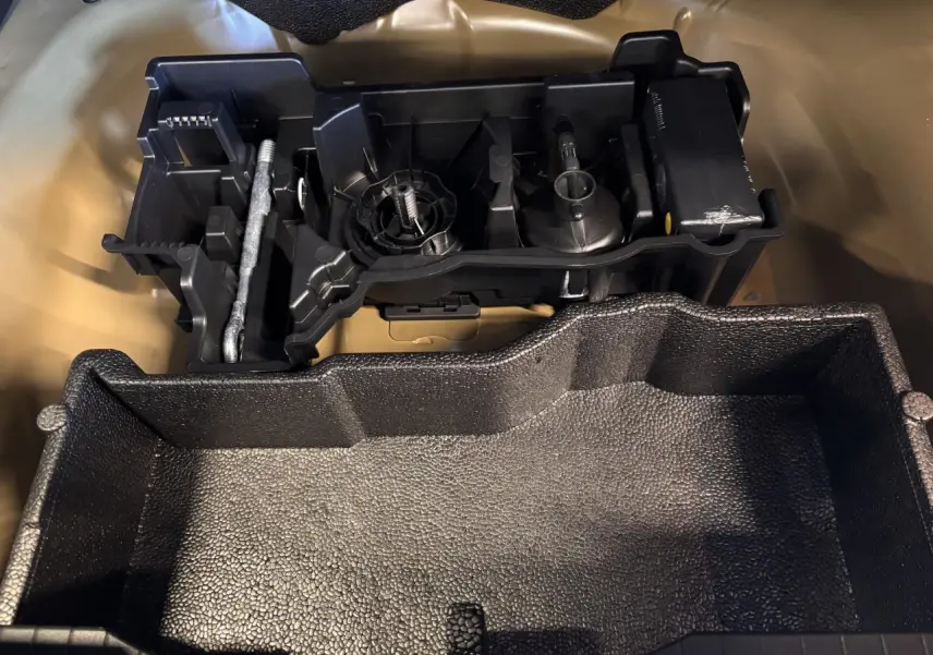 Kit de dépannage pneumatique noir dans le coffre du Peugeot 2008 gris hybride 2025, vue en plongée rapprochée.