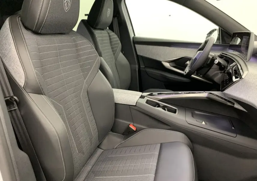 Vue intérieure côté gauche du Peugeot 3008 Hybrid 2026, sièges gris avec logo Peugeot brodé sur les appuie-têtes.