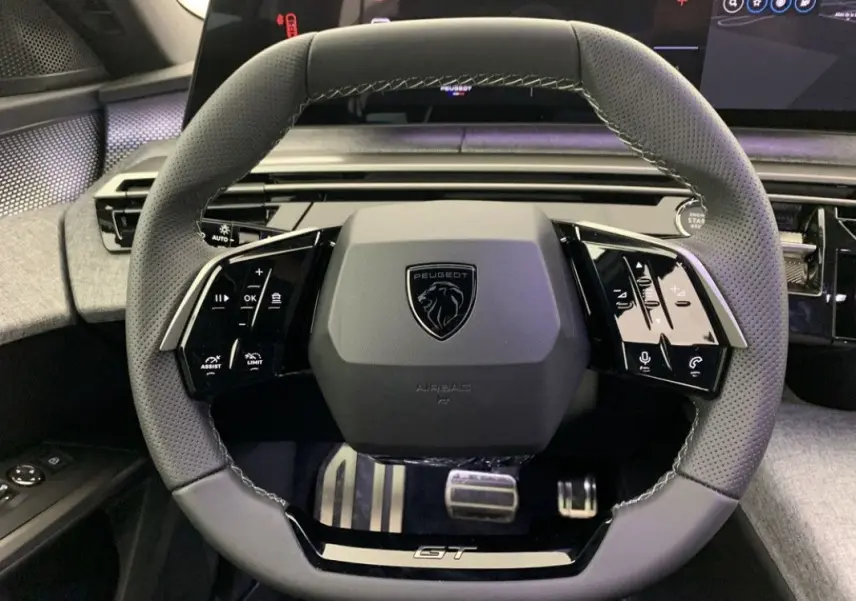 Vue rapprochée du volant gris perforé du Peugeot 3008 Hybrid 2026 avec logo central et commandes tactiles intégrées.
