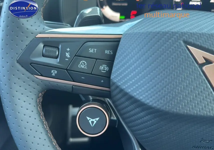 Gros plan sur le volant sport en cuir perforé avec commandes multifonctions et logo CUPRA sur fond carbone.