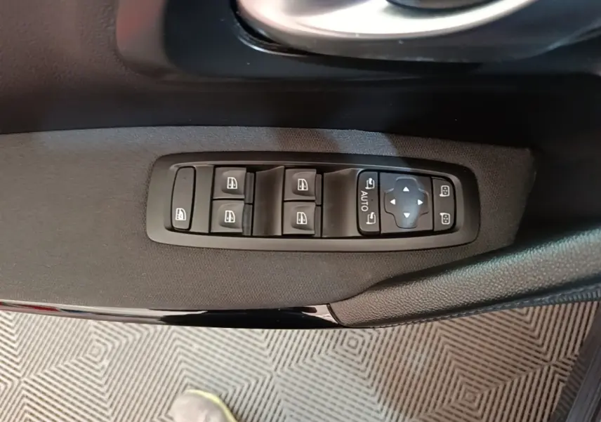 Gros plan sur les commandes électriques des vitres et des rétroviseurs côté conducteur d’une Renault Kadjar gris foncé.