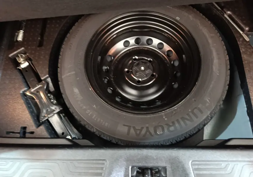 Gros plan sur la roue de secours noire et le cric dans le coffre d’un Renault Kadjar gris foncé.