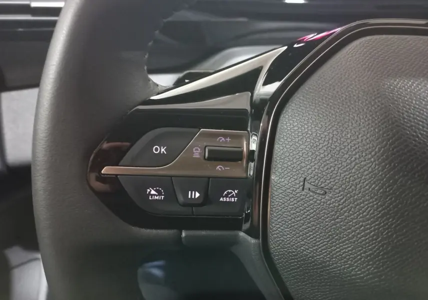 Gros plan sur le côté gauche du volant cuir de la Peugeot 308 PHEV 180 E-EAT8 Allure 2025 avec commandes intégrées.