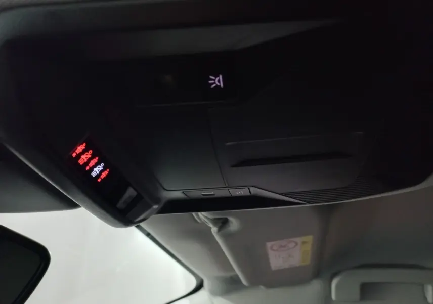 Vue intérieure du plafond avant de la Peugeot 308 PHEV 2025, avec commandes d’éclairage et affichage lumineux rouge.