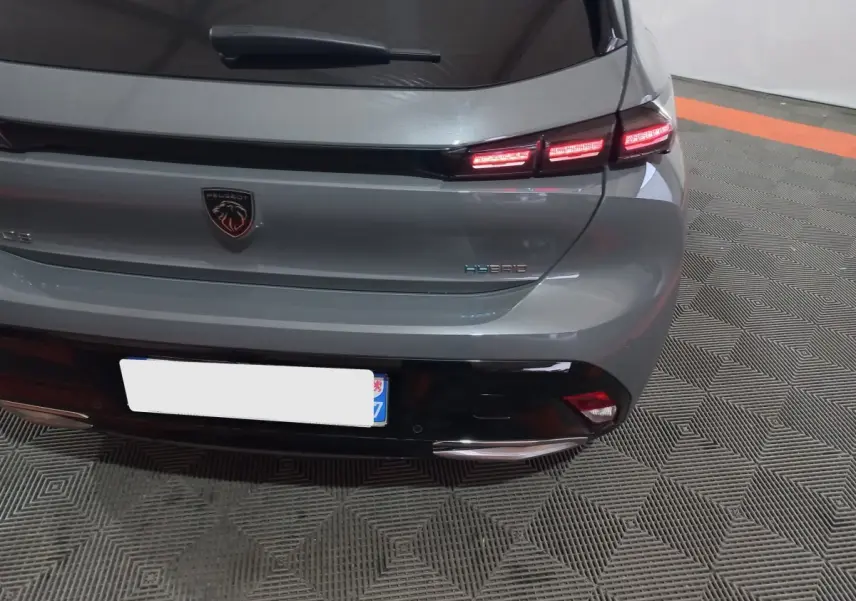 Vue arrière de la Peugeot 308 PHEV gris foncé avec feux LED allumés et logo hybride visible sur le coffre.