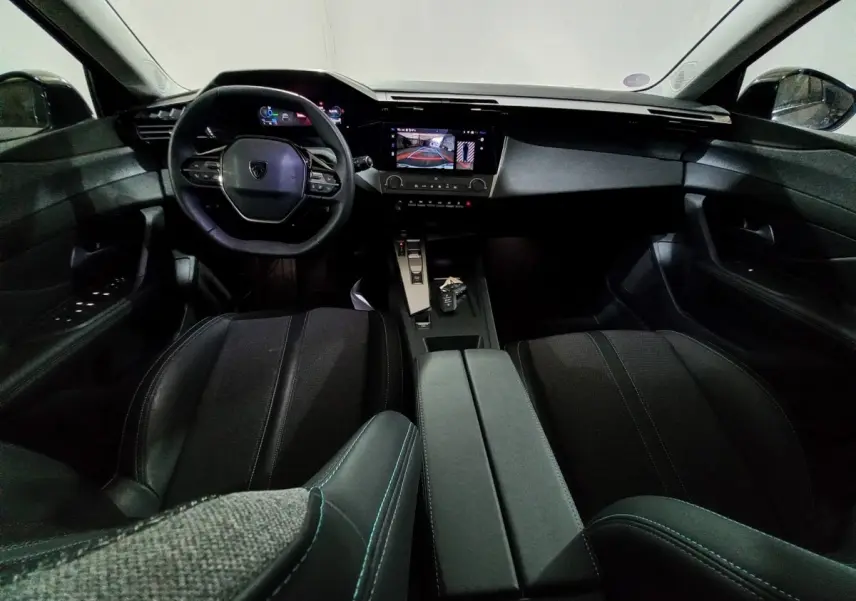 Intérieur noir de la Peugeot 308 PHEV 2025, vue avant centrée sur le volant, écran tactile et console centrale.