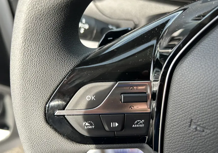 Gros plan sur les commandes noires du volant du Peugeot Partner Fourgon blanc 2025, avec boutons de limitation et assistance.