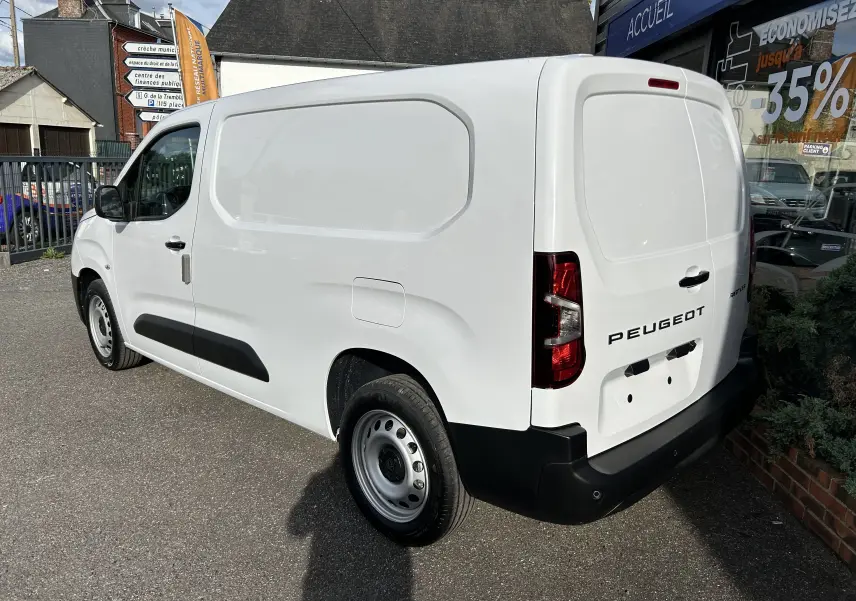 Vue 3/4 arrière droite d'un Peugeot Partner Fourgon blanc avec rétroviseurs noirs et plancher bois visible.